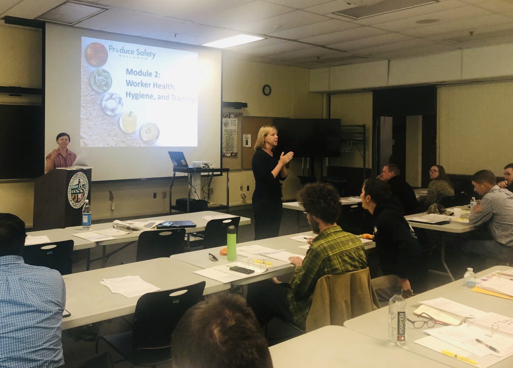 ALEI Specialist Nicole Cook (L)  and Managing Director Sarah Everhart (R) lead a Produce Safety Rule training in April. Image of two women standing and presenting a slideshow to a group of seated people.