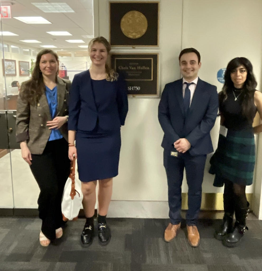 Four people standing, in business attire, next to a plaque